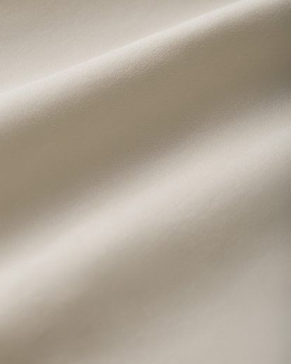 A close-up of draped off-white fabric with soft folds and a smooth matte texture.